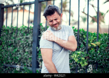 People, healthcare and medicine concept - unhappy man suffering from neck or shoulder pain outdoor Stock Photo