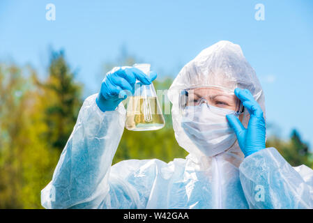 environmental chemist in protective clothing and glasses examines water from a forest lake Stock Photo