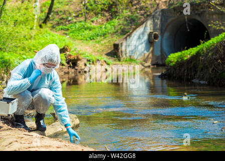 Scientist in protective suite taking water samples from the river Stock Photo