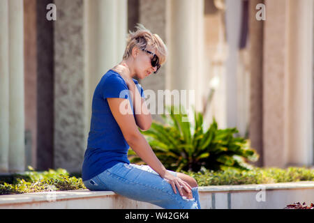 Woman holding her neck feeling pain while walking on the street. Health care, medicine and people concept Stock Photo