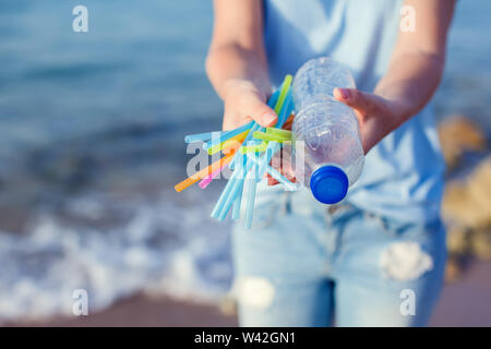 Woman holds plastic bottle and straws in hands on the beach. Plastic Pollution concept. Stock Photo
