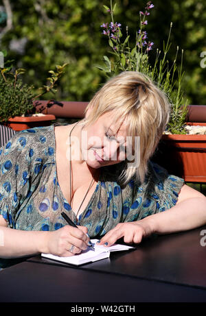 Woman and student sitting at table in bar, takes notes in notebook, learning and writes thoughts, writes book, she is preparing his doing homework. Stock Photo