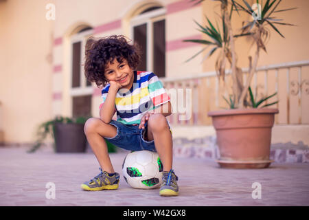 Little boy with curly hair with soccer ball outdoor. Children and entertainment concept Stock Photo