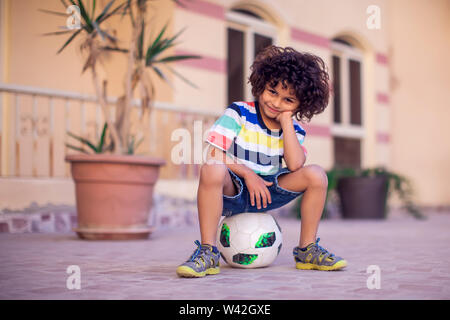 Little boy with curly hair with soccer ball outdoor. Children and entertainment concept Stock Photo