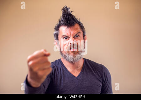 Closeup portrait of an angry adult man with a beard and iroquois shows fist. People and emotions concept Stock Photo