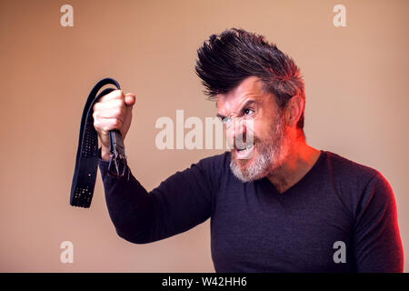 Angry bearded man holds belt in hand. Emotions and family violence concept Stock Photo