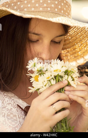 pretty girl in sun hat with camomile bouquet smells flowers, toned image Stock Photo