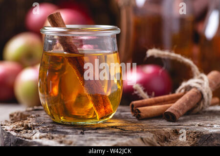 Closeup of a glass of apple cider and cinnamon sticks on a rustic wood surface with red apples in background Stock Photo