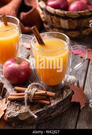 Cup of apple cider and cinnamon stick with fresh red apples on a rustic wooden surface Stock Photo