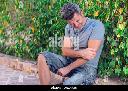 Man feels strong pain in elbow while walking on the street. People, healthcare and medicine concept Stock Photo