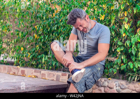 Man feels strong foot pain outdoor. People, healthcare and medicine concept Stock Photo