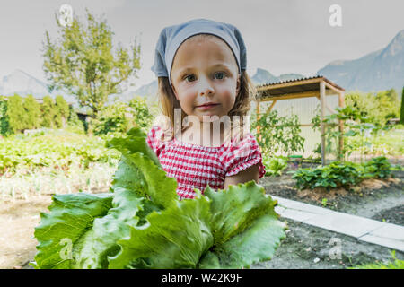 young girl proudly holding an organic lettuce she just harvested from her vegetable patch in the Swiss countryside Stock Photo