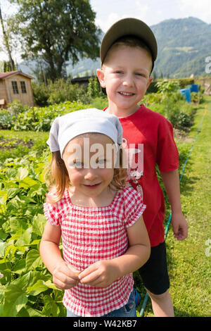 young girl and older borther proudly stad in in front of their vegetable patch in the Swiss countryside Stock Photo
