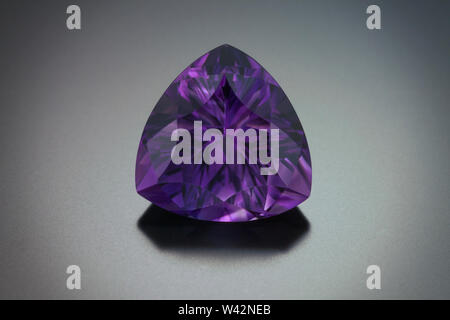 A large fantasy cut pincushion triangle shape amethyst gemstone on a dark background. Stock Photo