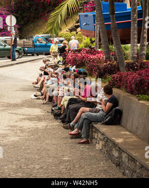 A row of people sitting down outside eating sandwiches after taking a walk. Stock Photo