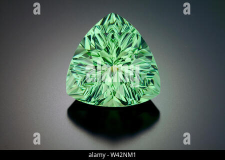 A large fantasy cut pincushion triangle shape peridot gemstone on a dark background. Stock Photo
