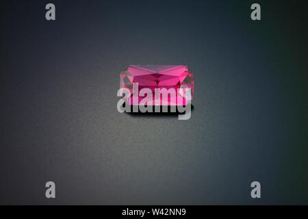 A small faceted, emerald cut ruby sits on a reflective black background. Stock Photo