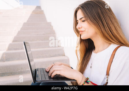 Front view of a happy student girl working with a laptop in the stairs of an university campus Stock Photo