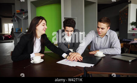 Cheerful and active staff of company, two men and women, with smiles on their faces and in good spirits, completed work process and lay their hands on Stock Photo