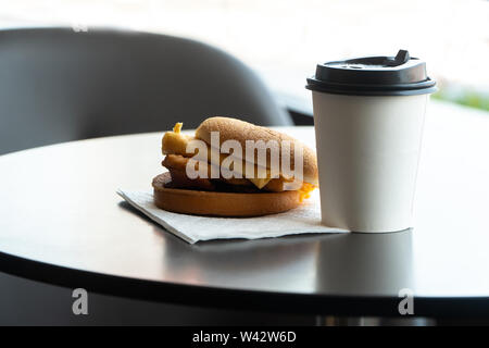 Bacon and Omelette Hamburger on the paper with White paper coffee mug on the table in fast food restaurant Stock Photo