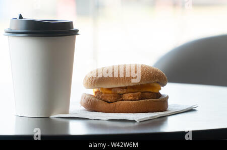 Bacon and Omelette Hamburger on the paper with White paper coffee mug on the table in fast food restaurant Stock Photo