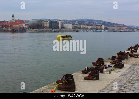 The 'River Ride' amphibious, sightseeing tourist bus floats in the Danube river past the 'Shoes On The Danube Bank' memorial. Stock Photo