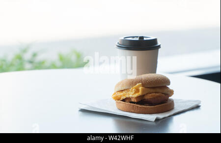 Bacon and Omelette Hamburger on the paper with White paper coffee mug on the table in fast food restaurant Stock Photo