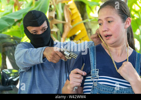 Man with masked robber and threatening with gun to scared woman in car parking. The victim of the crime was terrified and have anxiety symptoms. Stock Photo