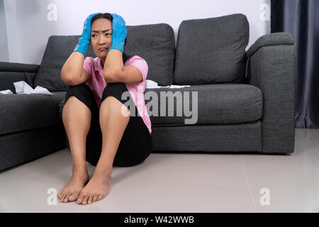 Middle-aged woman Wearing blue rubber gloves for cleaning and sitting on the floor. She was tired of cleaning the house. Stock Photo