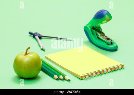 Compass, color pencils, notebook, apple and stapler on green background. Back to school concept. School supplies. Shallow depth of field. Stock Photo