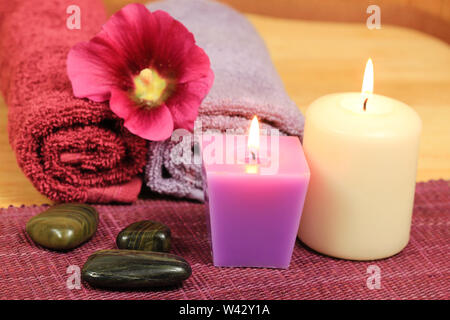 Spa composition in heath color with burning candles, stones and holyhock flower Stock Photo