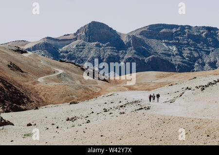 Three hikers walk on trail in rocky and volcanic landscape Stock Photo