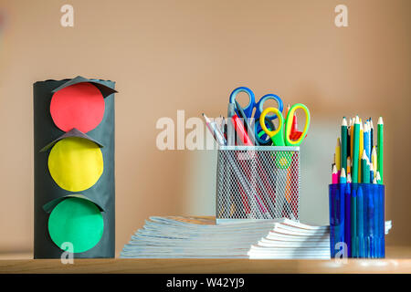 Stack of notebooks, colorful drawing pencils, paper toy traffic lights and stationery arrangement on copy space background. Stock Photo
