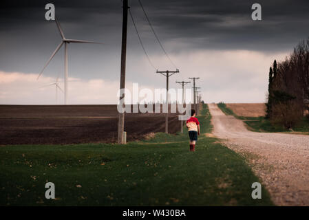 small boy standing near a dirt road on a wind farm Stock Photo