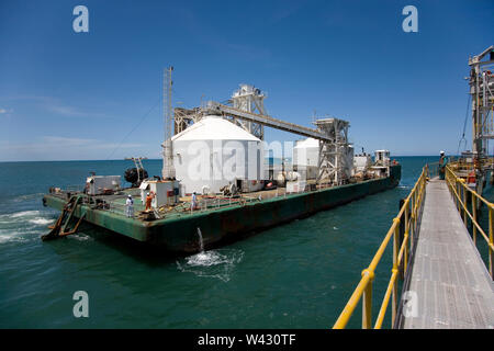 Mining, managing & transporting of titanium mineral sands. Custom built barge arriving at jetty to load up with mineral before transfer to OGV at sea. Stock Photo
