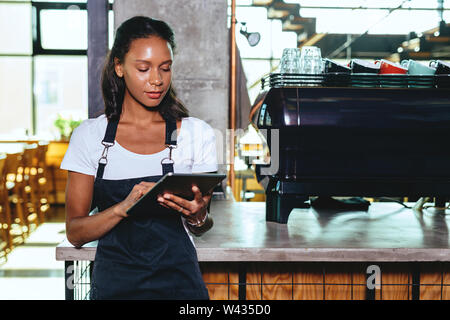 Young barista using digital tablet. Waitress standing by the coffee machine. Stock Photo