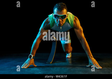 Athlete with disabilities or amputee on black background in neon light. Professional male runner with leg prosthesis training and practicing in studio. Disabled sport and healthy lifestyle concept. Stock Photo