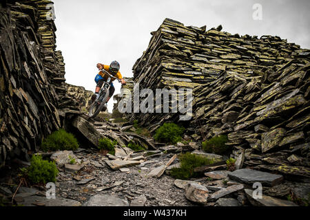 A mountain biker riding on a rocky mining path between ancient dry-stone walls.