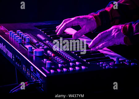 Closeup of male hands playing a modern synthesizer keyboard under stage lighting. Stock Photo