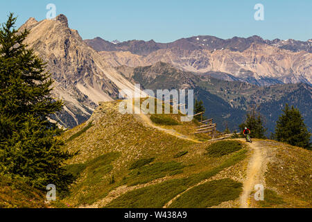 SAUZE D'OULX, ITALY - AUGUST 7, 2010. A man rides a mountain bike along a ridgeline trail with high Alpine peaks in the background Stock Photo