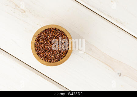 Lot of whole raw red quinoa seeds in a wooden bowl flatlay on white wood Stock Photo