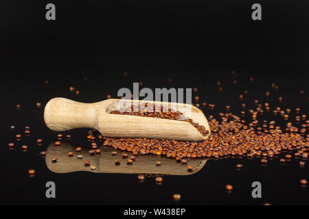 Lot of whole raw red quinoa seeds with wooden scoop isolated on black glass Stock Photo