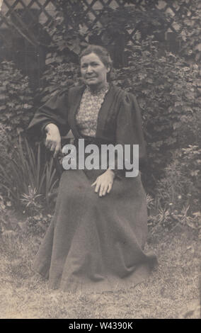 Vintage Postcard of an Edwardian / Early 20th Century Lady Sat in a Leafy Garden Stock Photo