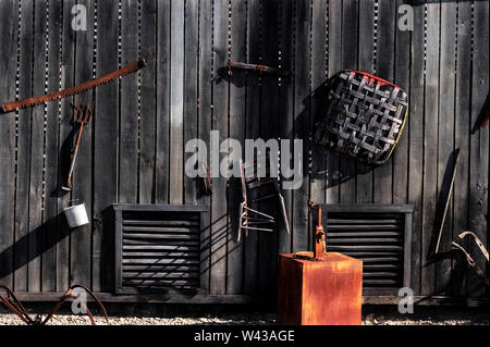 The side of a wooden slab buildings exterior wall with old no longer used items hanging on it. Stock Photo