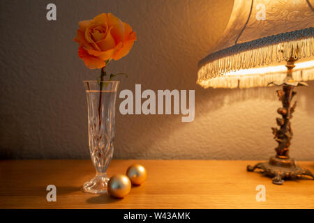 A large Whisky Mac Hybrid Tea Rose cut flower in a cut glass vase lit by a table lamp Stock Photo