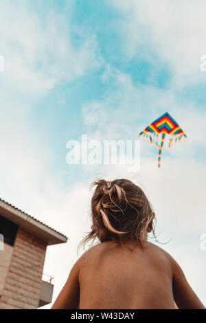 Happy child launches a kite, baby looking up at a multi-colored kite soaring in the sky, happy childhood, kid enjoying summer holidays Stock Photo