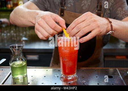 Bartender is adding lemon zest to the cocktail at bar counter Stock Photo
