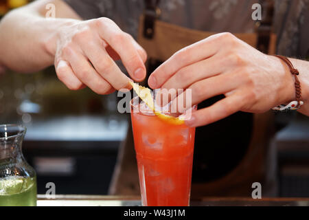 Bartender is adding lemon zest to the cocktail at bar counter Stock Photo