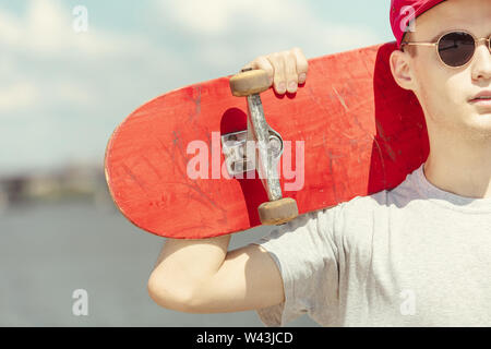 Skateboarder resting after riding at the city's street in sunny day. Young man in sneakers and cap with a longboard on the asphalt. Concept of leisure activity, sport, extreme, hobby and motion. Stock Photo