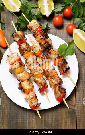 Grilled chicken on bamboo skewers. Vegetables and herbs on wooden table, top view